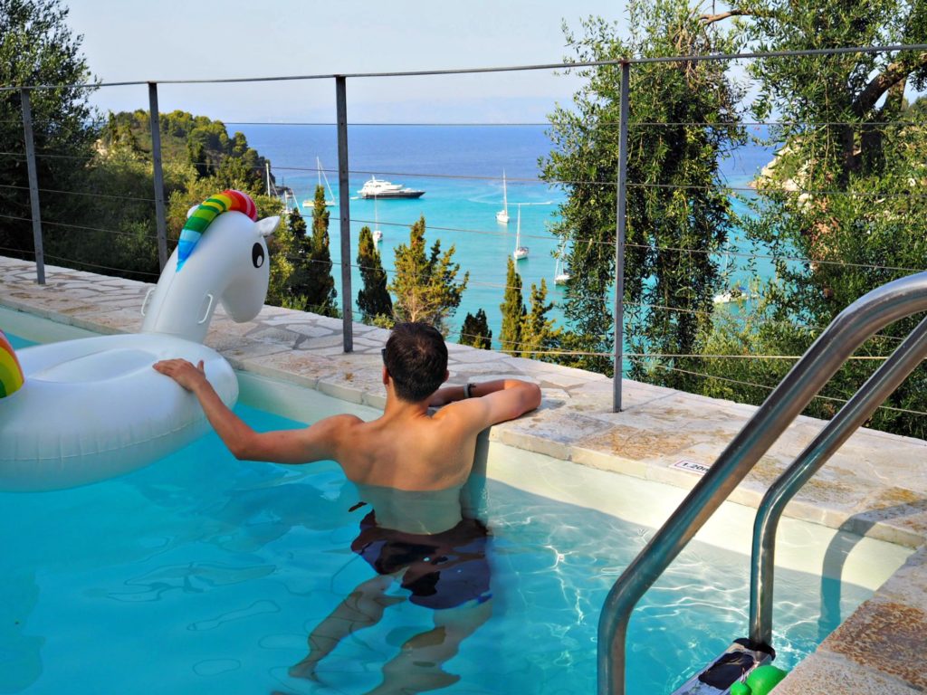 Boy with inflatable unicorn pool toy looking over side of pool at view of Lakka bay. Copyright © 2017 mapandfamily.com 