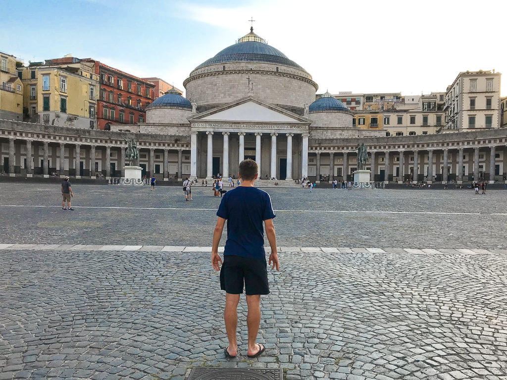 Back view of boy facing two statues on opposite side of large cobbled piazza