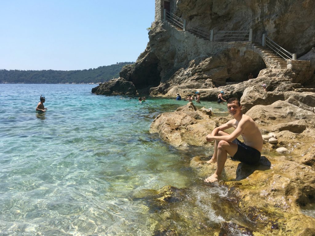 Dubrovnik kayaking tour: boy sitting on rocks at the water's edge. Copyright©2017 mapandfamily.com
