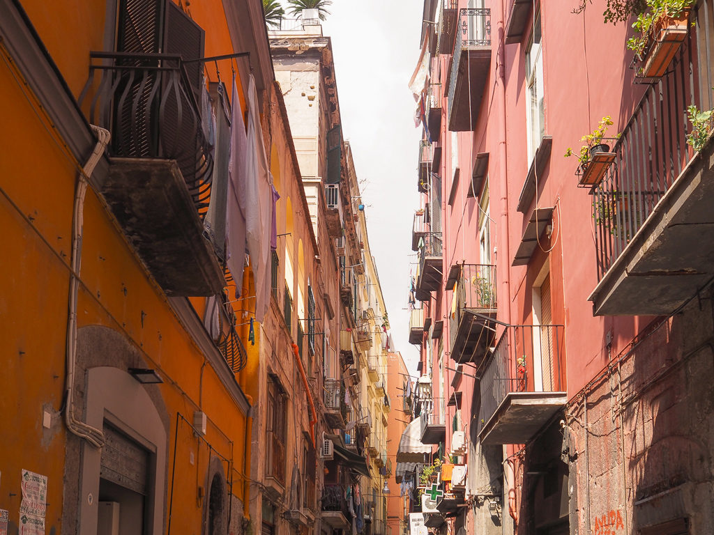 A narrow street with ochre and pink buildings and balconies in historic centre of Naples