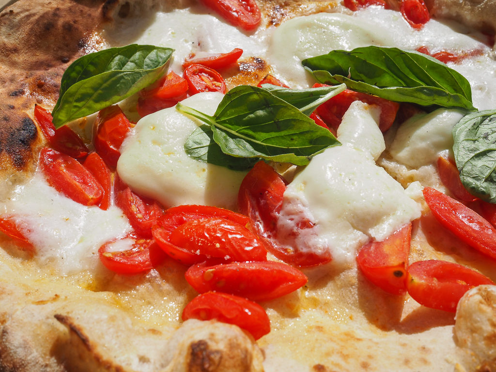 Close up of pizza with tomatoes, pale cheese and basil leaves. 