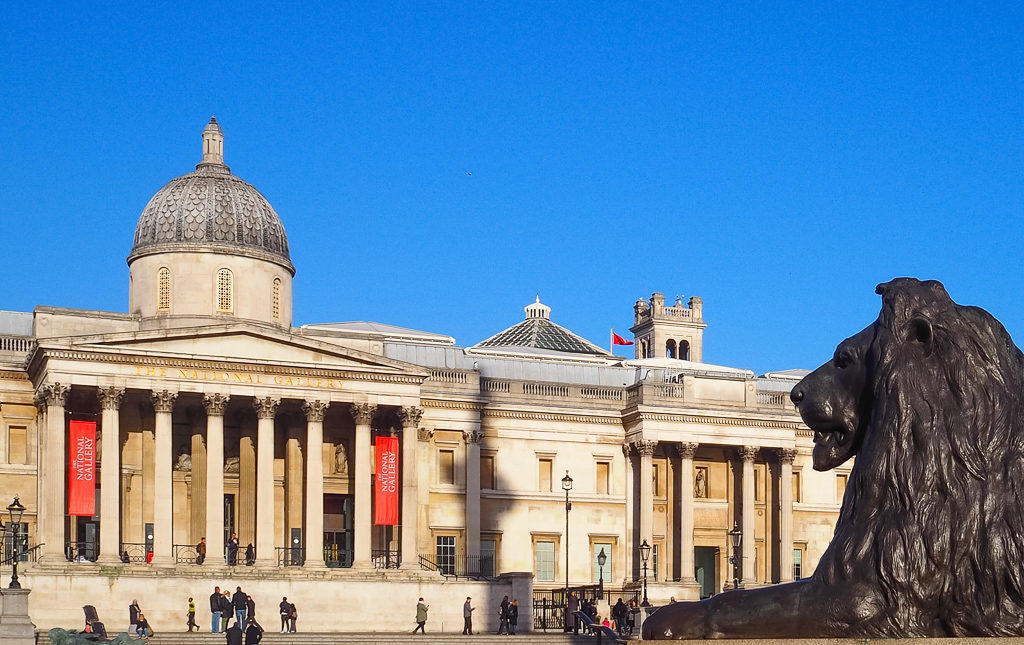 Exterior of National Gallery in Trafalgar Square with statue of lion in foreground. Copyright ©2019 mapandfamily.com 