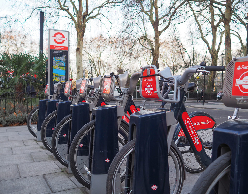 Row of grey and red Santander bikes in docking station. Copyright ©2019 mapandfamily.com 
