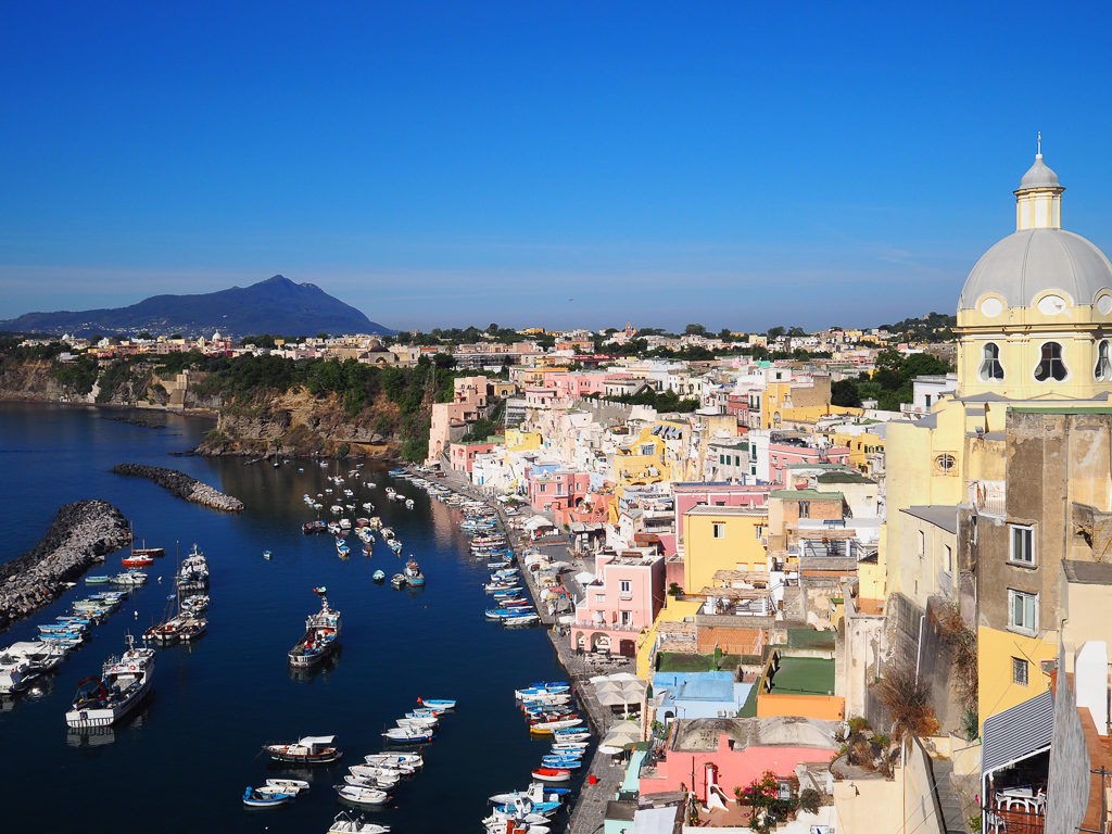 Day trip to Procida. View of pink and yellow coloured houses on harbour. Copyright©2019 mapandfamily.com 