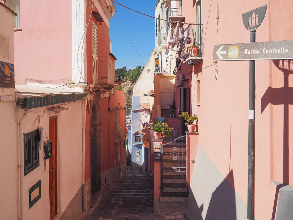Corricella, Procida. Narrow staircase leading to harbour with pink walls on either side. Copyright©2019 mapandfamily.com 