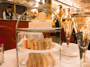 Glasses of champagne and a stand of cakes in a glittering room at the Cafe Royal.Copyright ©2019 mapandfamily.com
