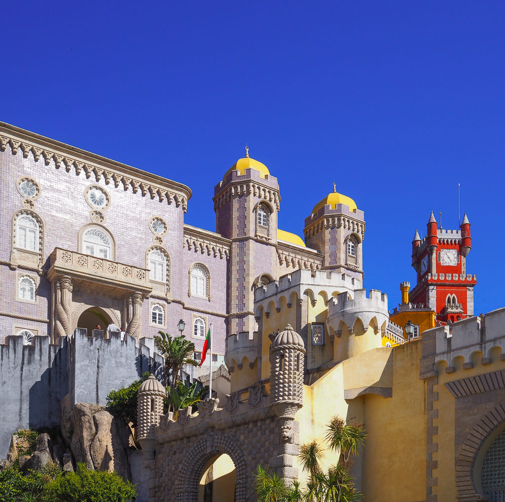 Things to do in Sintra: see the mauve, yellow and red turrets and towers  of Pena Palace, here against a blue sky  Copyright@2025 NancyRoberts