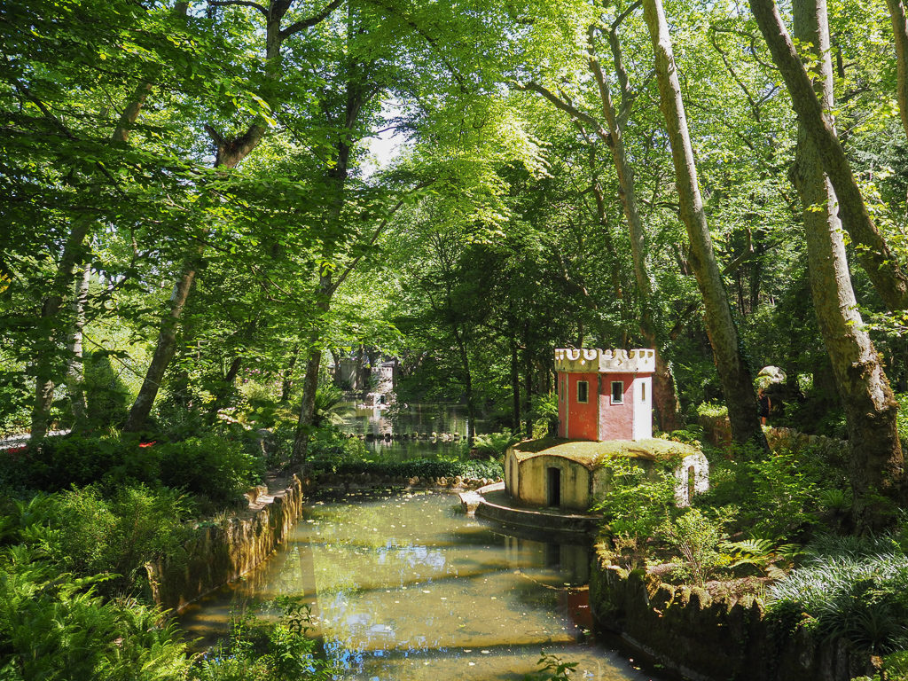 A small lake surrounded by trees with an elaborate duck house built like a castle. Copyright@2025 NancyRoberts