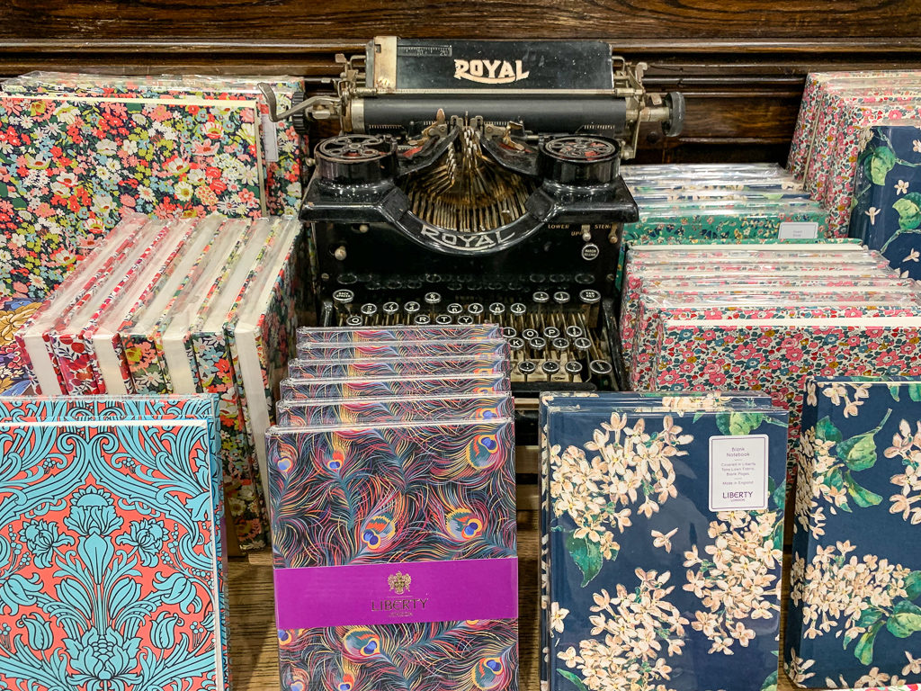 Floral patterned Liberty fabric notebooks and journals displayed around an antique typewriter.Copyright ©2019 mapandfamily.com