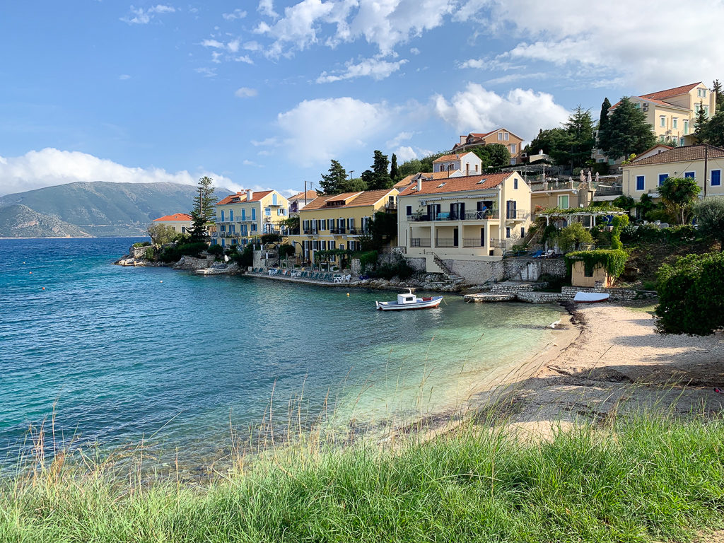 The small town beach in Fiskardo with villas overlooking the bay. Copyright@2019 mapandfamily.com 