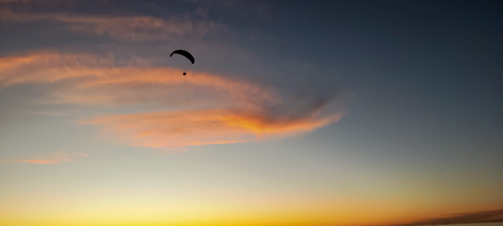 A paraglider silhouetted against a sky streaked with apricot as sun sets. Copyright@2023 reserved to photographer via mapandfamily.com