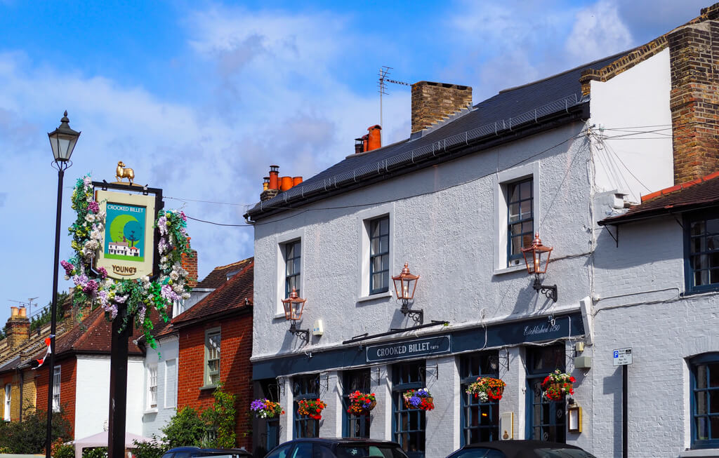 Exterior of whitewashed pub with hanging baskets, pub sign and old street lantern. Copyright@2023mapandfamily.com 