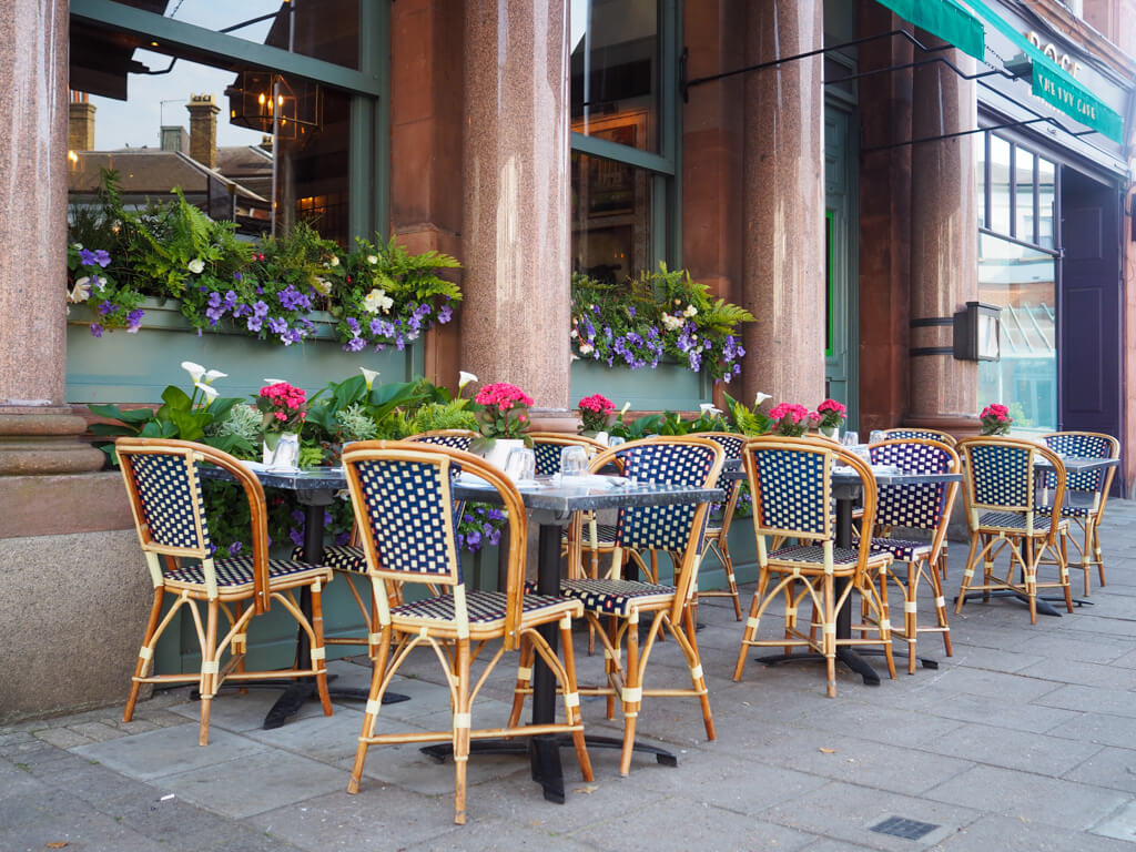 French style cafe tables and chairs outside The Ivy Cafe with window boxes above. Copyright@2023 mapandfamily.com 