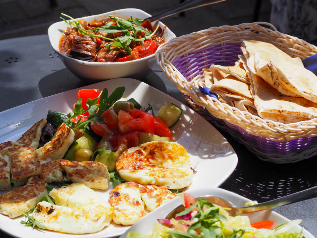 A group of mezze dishes at one of the Wimbledon village restaurants, showing pitta bread in a basket, salad and grilled halloumi. Copyright@2024 Nancy Roberts