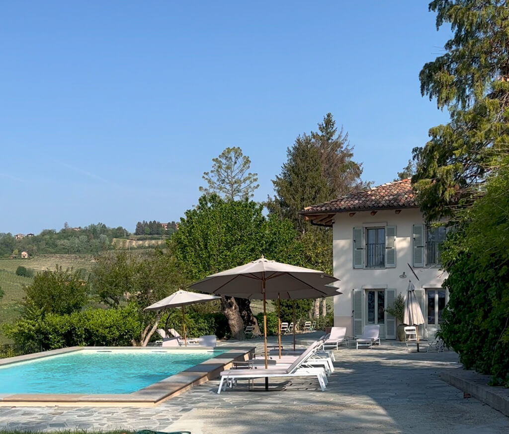 View of Italian farmhouse with pale green shutters, swimming pool, loungers and parasols. Copyright@2023mapandfamily.com 