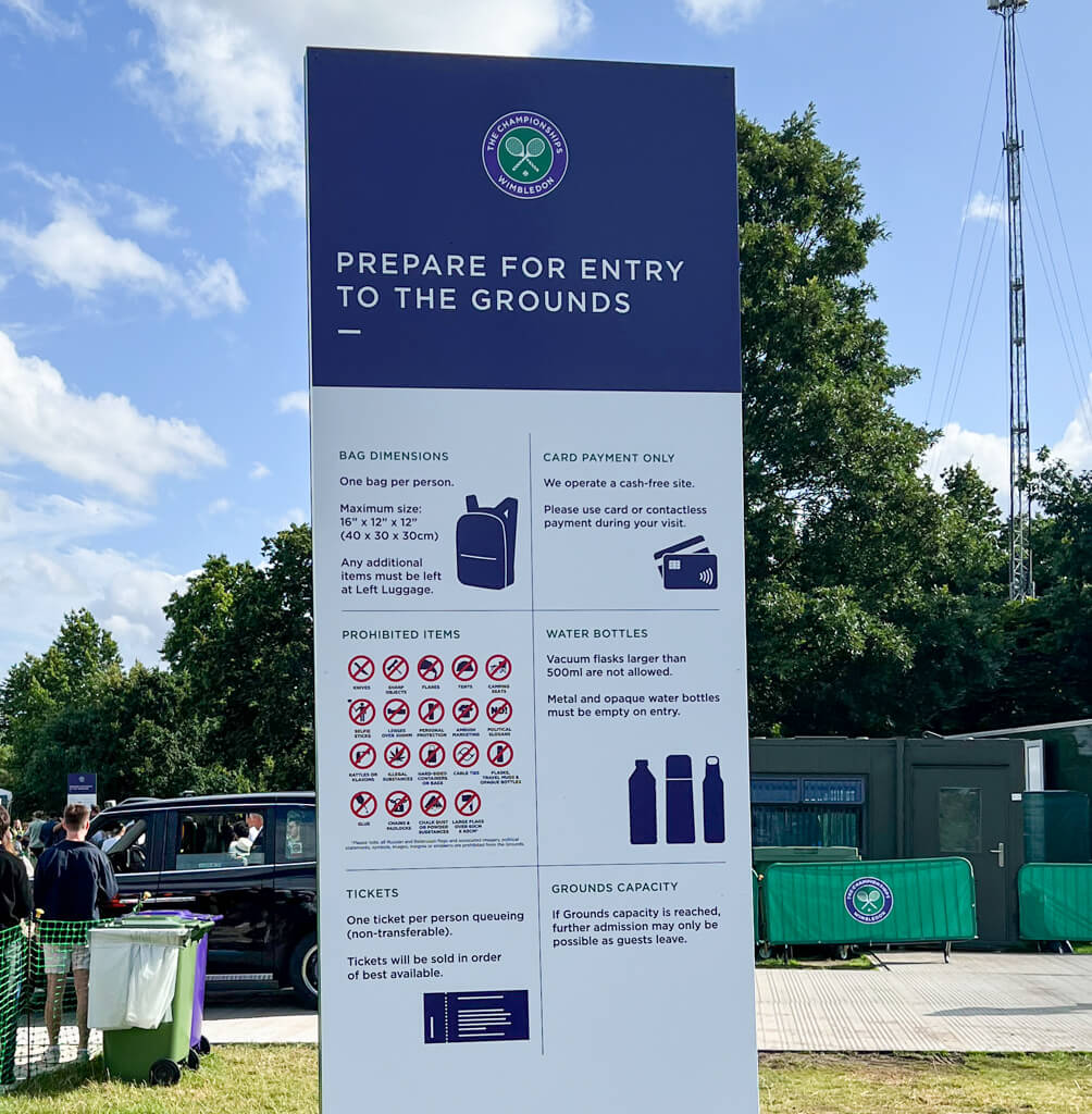 Large dark blue and white sign in a park showing what items can and cannot be taken into Wimbledon grounds. Copyright@2023mapandfamily.com 