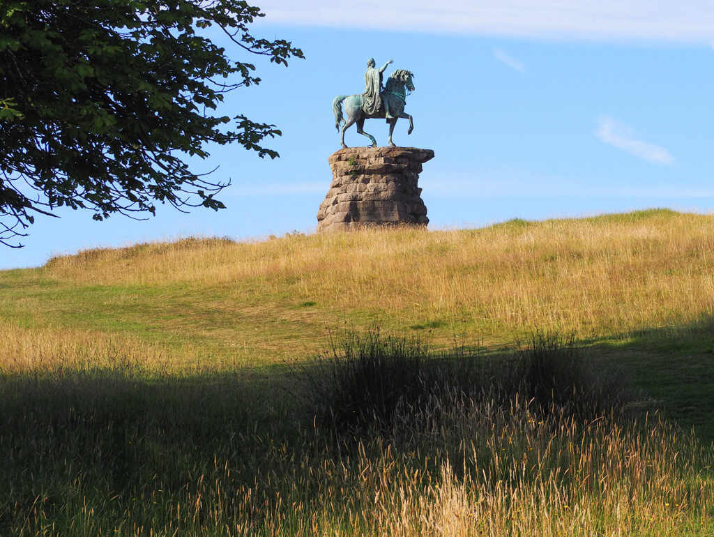 A bronze statue of horse and rider on a stone plinth on a rise of land. Copyright@2023 mapandfamily.com