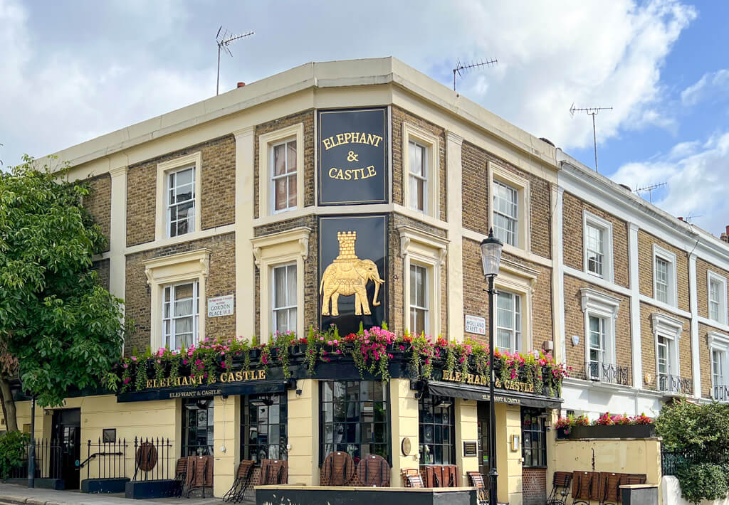 The Elephant and Castle pub has a large golden sign with an elephant and howdah above a row of window boxes. Copyright@2023 mapandfamily.com