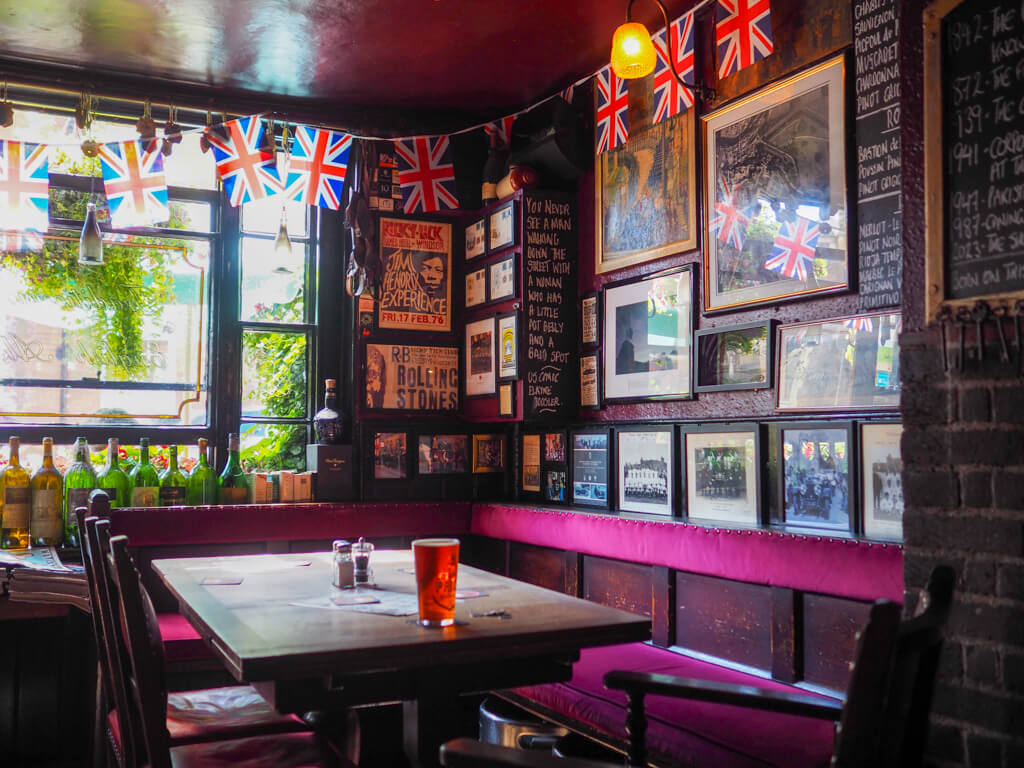 Interior of pub with a pint of beer on table, lots of photos on wall and flags hanging like bunting around cornice.Copyright@2023 mapandfamily.com 