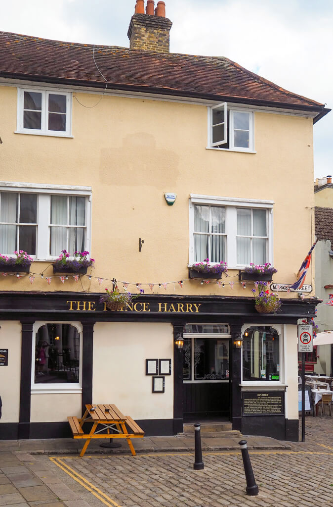 Exterior of yellow painted pub with a black and gold sign reading The Prince Harry. Copyright@2023 mapandfamily.com 