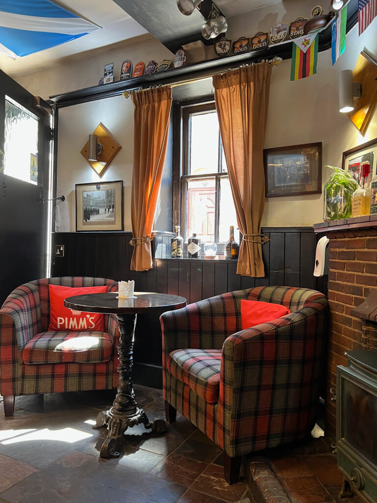 Cosy interior of pub with tartan armchairs and curtains at window. Copyright@2023 mapandfamily.com 