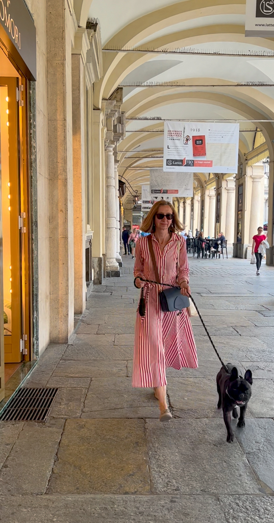 Woman in red striped dress and small dog in colonnaded shopping street in Turin. Copyright@2023 mapandfamily.com