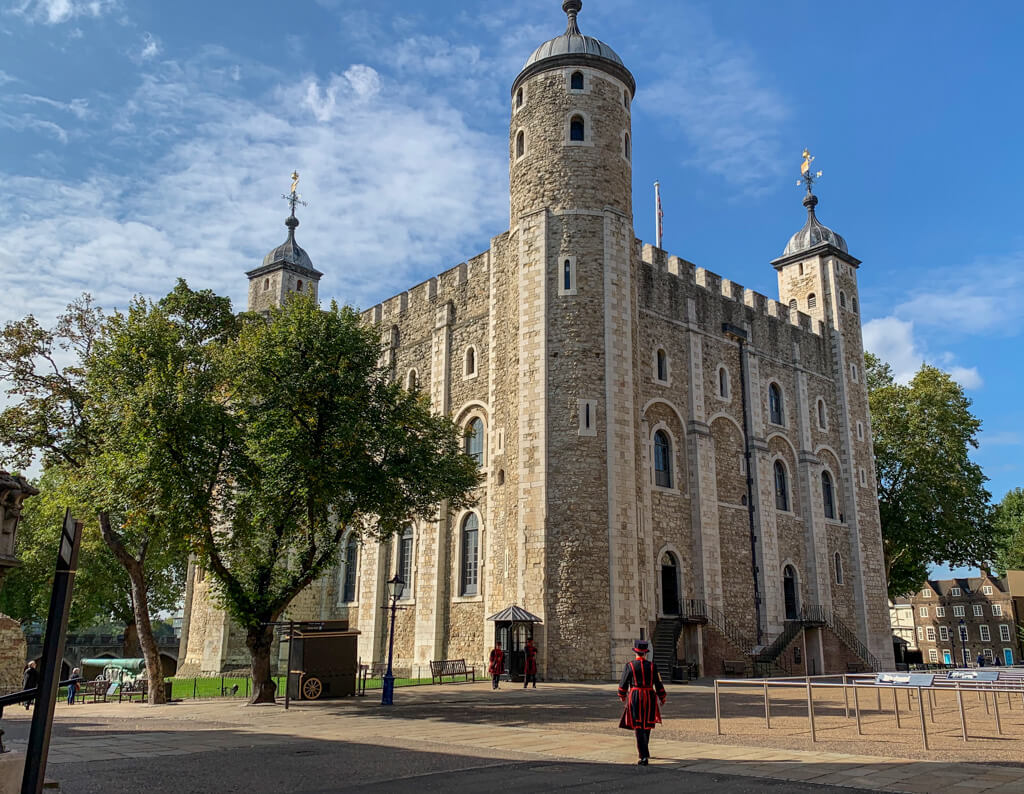 The tall white tower keep in the Tower of London with a yeoman warder walking towards it. Copyright@2023mapandfamily.com 