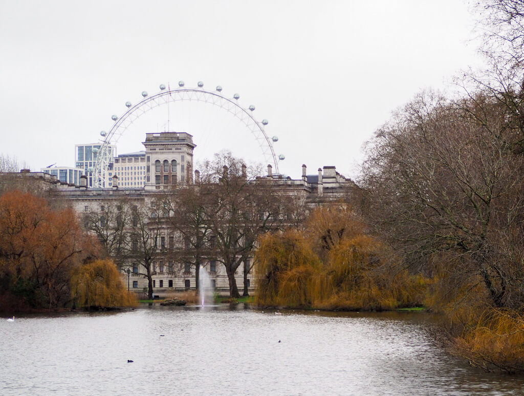 View from bridge in St James's Park towards the London Eye. A grey morning with dark gold foliage and bare branches. Copyright @2023 mapandfamily.com 