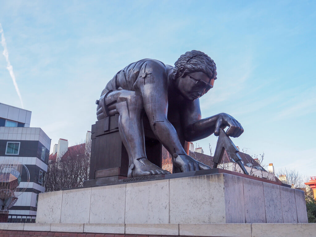 Modern statue of Newton bent over his work on plinth outside British Library. Copyright@2023 mapandfamily.com