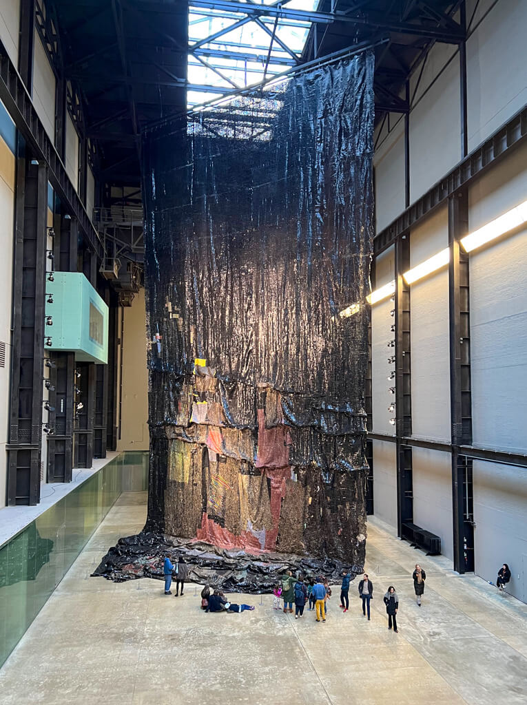 Turbine Hall with huge hanging that drapes onto the floor overshadowing the people gathered around it. Copyright@2023 mapandfamily.com