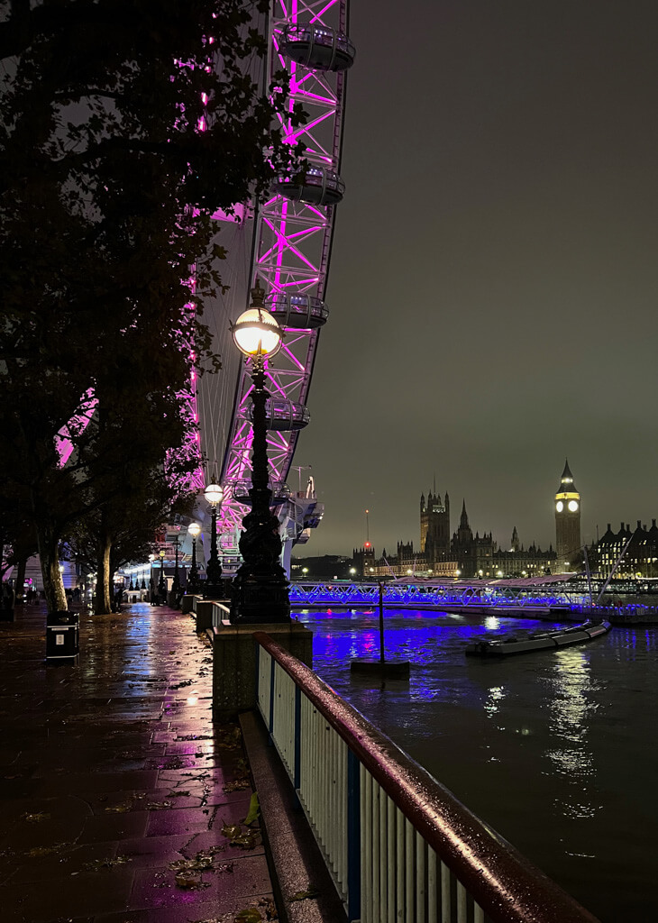 The London Eye with purple lighting at night with Big Ben in distance. Copyright@2023 mapandfamily.com