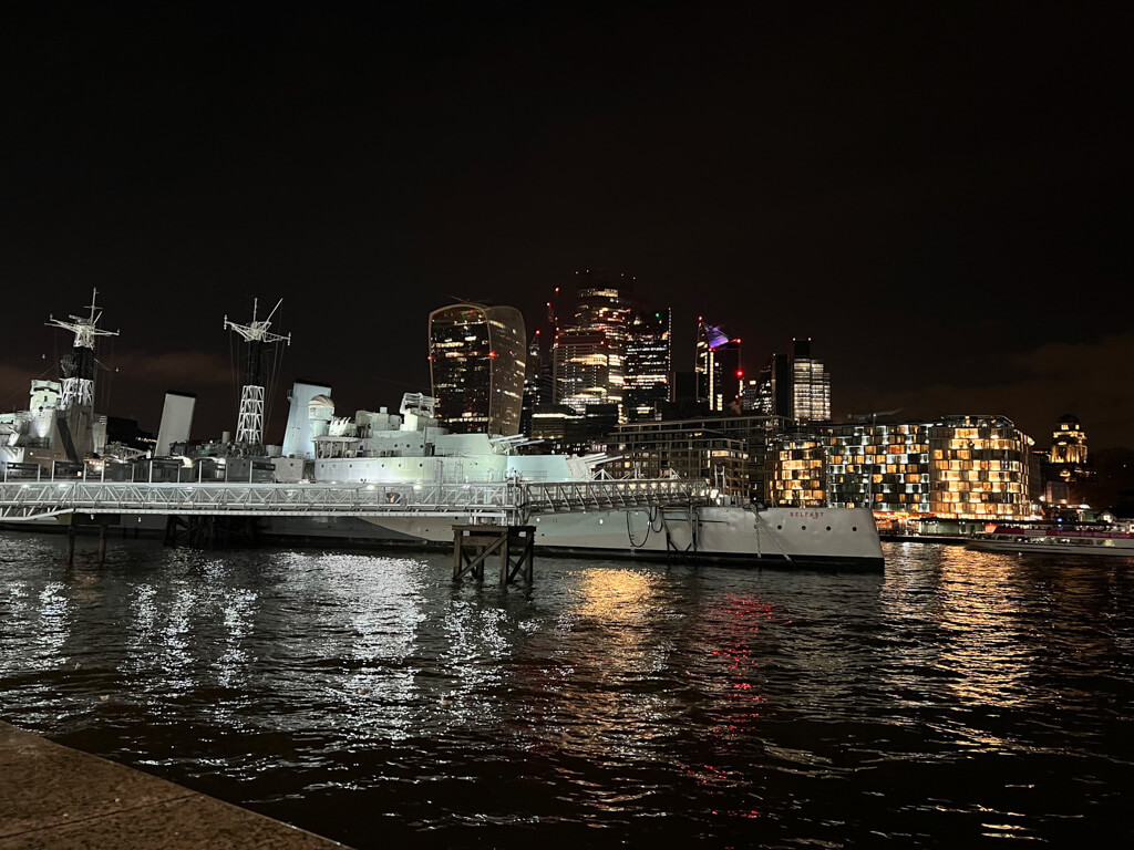 HMS Belfast with the city skyscrapers in background, illuminated at night. Copyright@2023mapandfamily.com