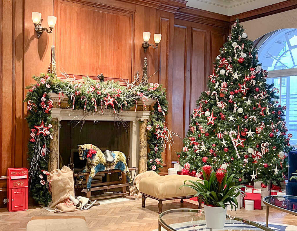 Reception at hotel with large Christmas tree and rocking horse in front of period fireplace. Copyright@2023 mapandfamily.com