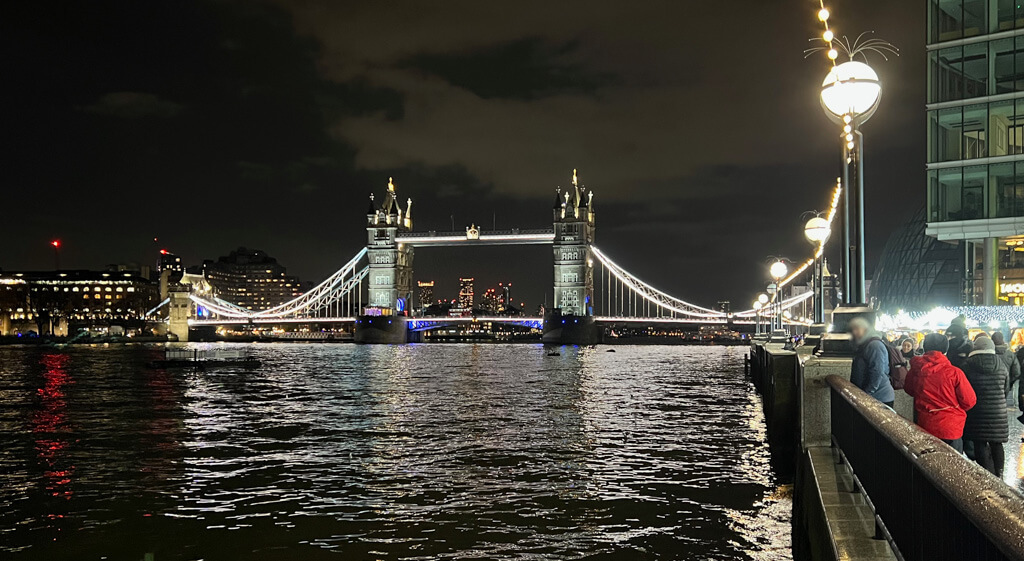 Beside the river at night at the London Bridge Christmas market with view of Tower Bridge. Copyright@2023 mapanfamily.com 