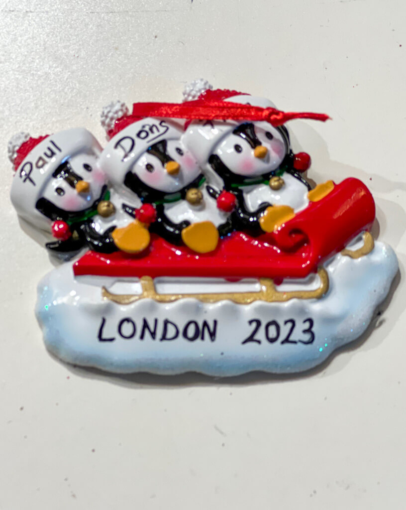 Tree ornament of penguins on a sled personalised with names and London 2023 script. Copyright@2023 mapanfamily.com 