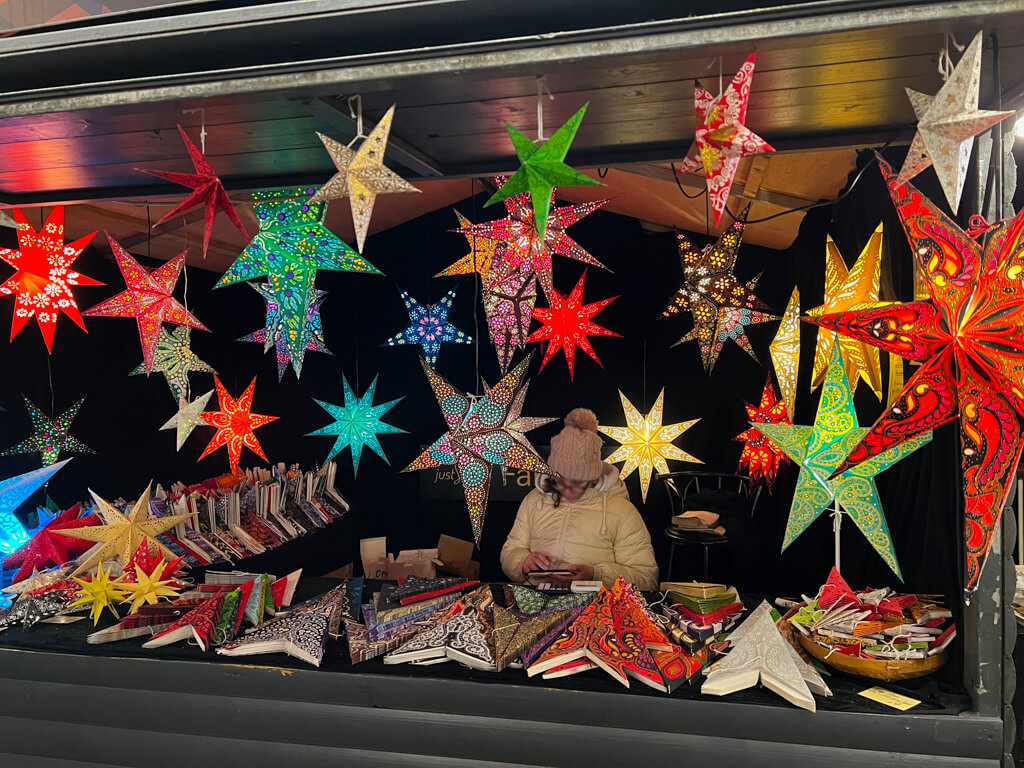 Multicoloured folded paper star decorations hanging in wooden cabin. Copyright@2023 mapandfamily.com