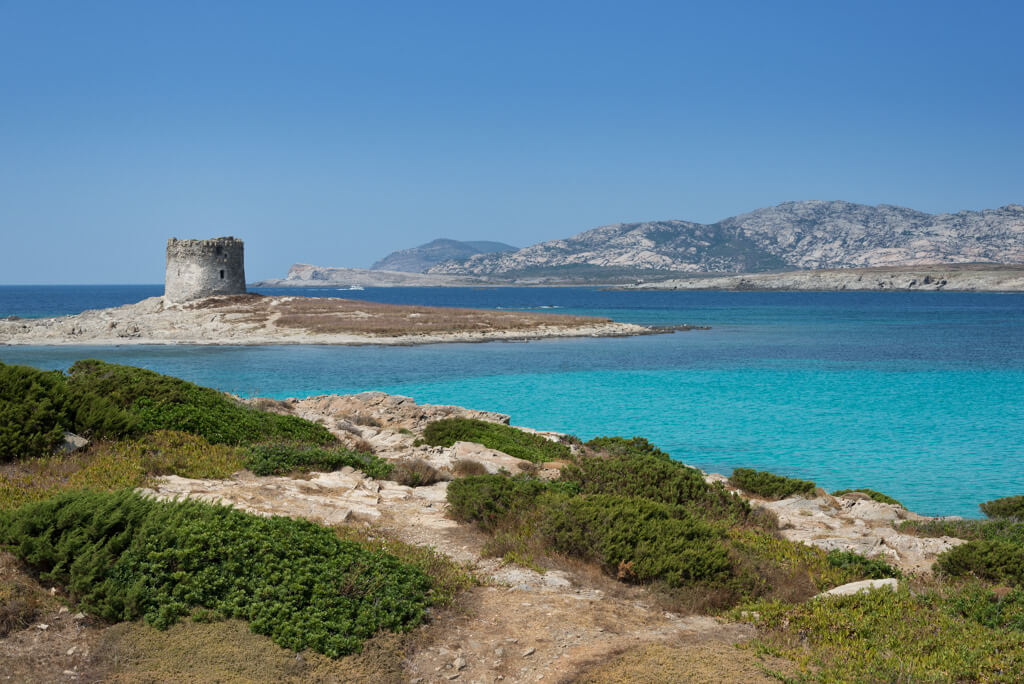 Turquoise sea and a historic tower are the view from La Pelosa beach in Sardinia.