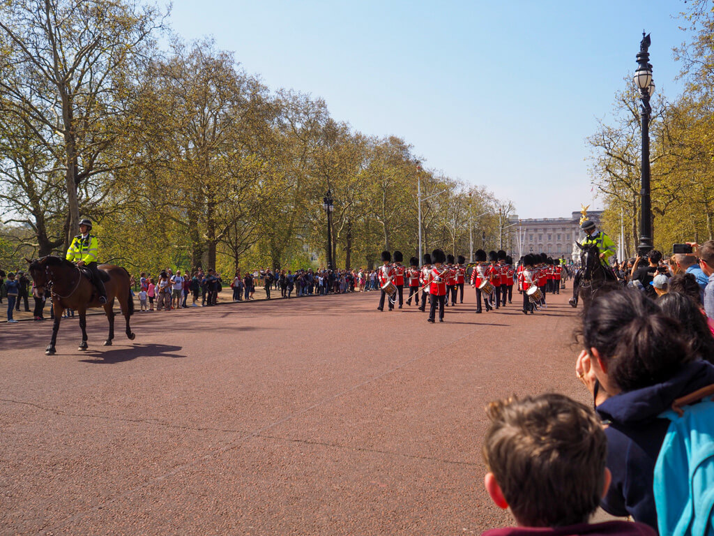 Troops wearing red tunics and bearskin hats march on the Mall with a police escort. Copyright@2024mapandfamily.com 