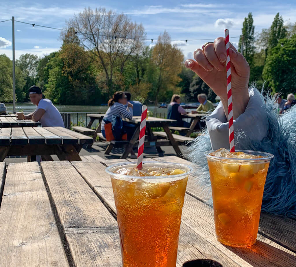 Sunny May day on outdoor terrace with plastic cups of Pimms with straws. Copyright@2024NancyRoberts