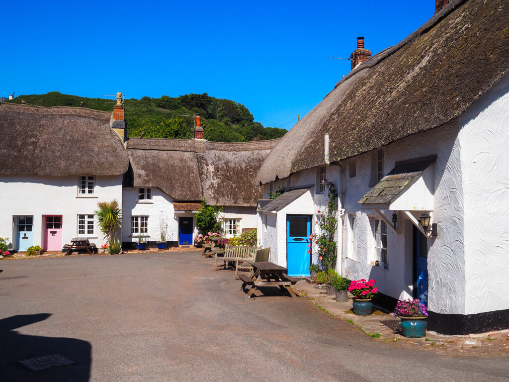 Quintessential English countryside view of thatched cottages with colourful painted doors in a sunny square. Copyright@2025NancyRoberts