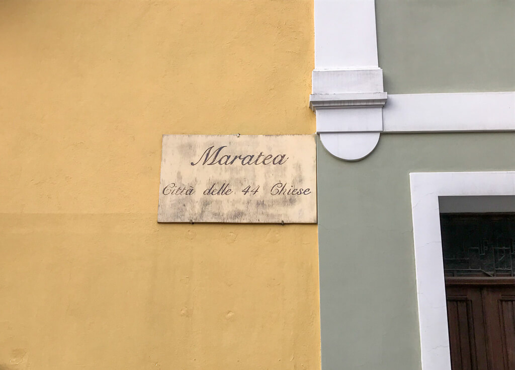A decorative Italian sign on a yellow plaster wall describing Maratea as the city of 44 churches. Copyright@2024 reserved to the photographer via mapandfamily.com 