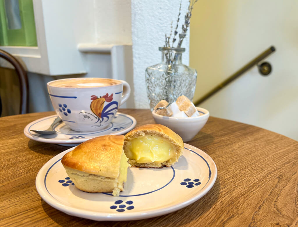 A painted ceramic cup, saucer and plate with cappuccino and sweet pie with custard filling. Copyright@2024mapandfamily.com 