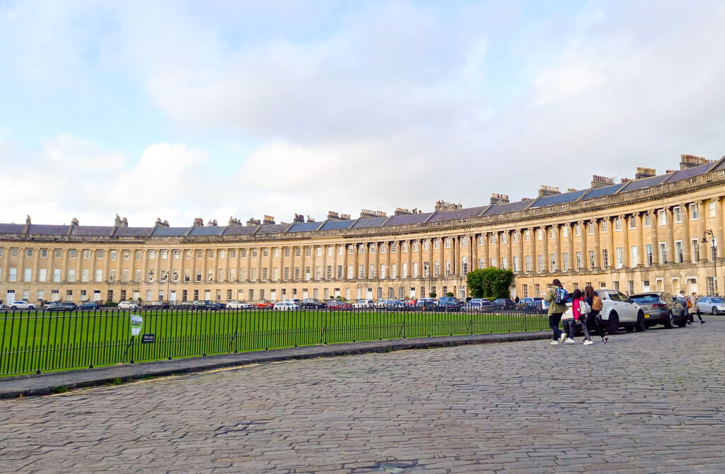 A long curving crescent of grand terraced houses in pale golden stone in Bath. Copyright@2024 mapandfamily.com