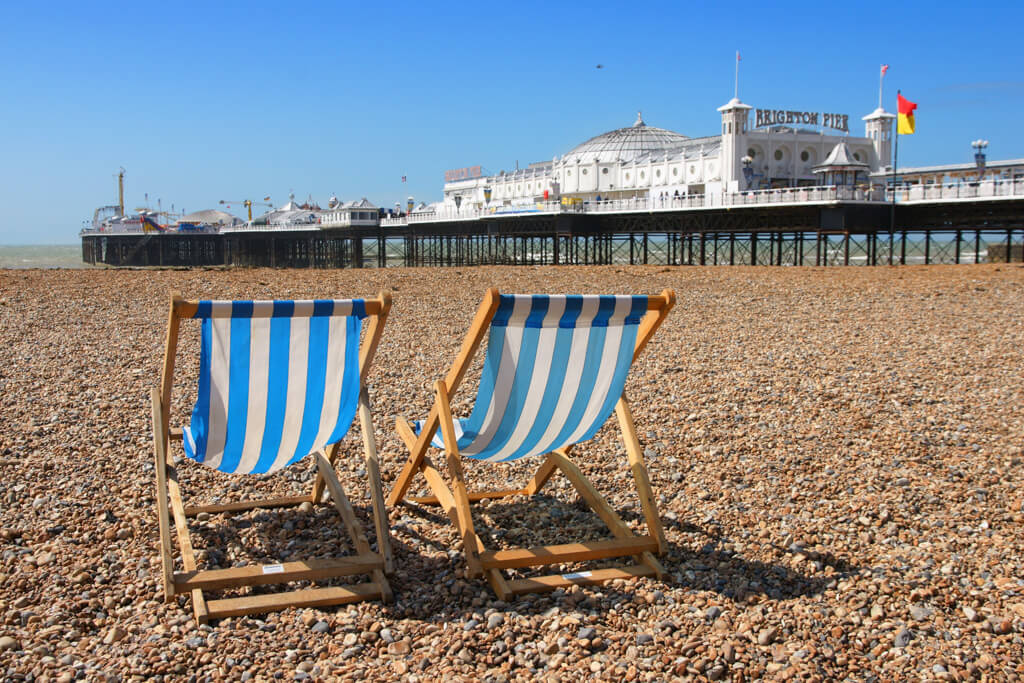 Brighton is one of the nearest cities to London. The image shows its popular pebble beach,stripy deckchairs and Brighton pier.in the background..  