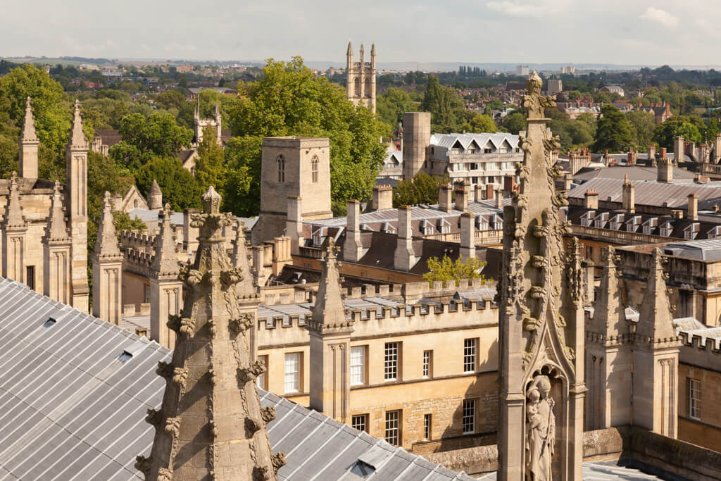 The skyline of Oxford with many spires and turrets along with mature green trees. 