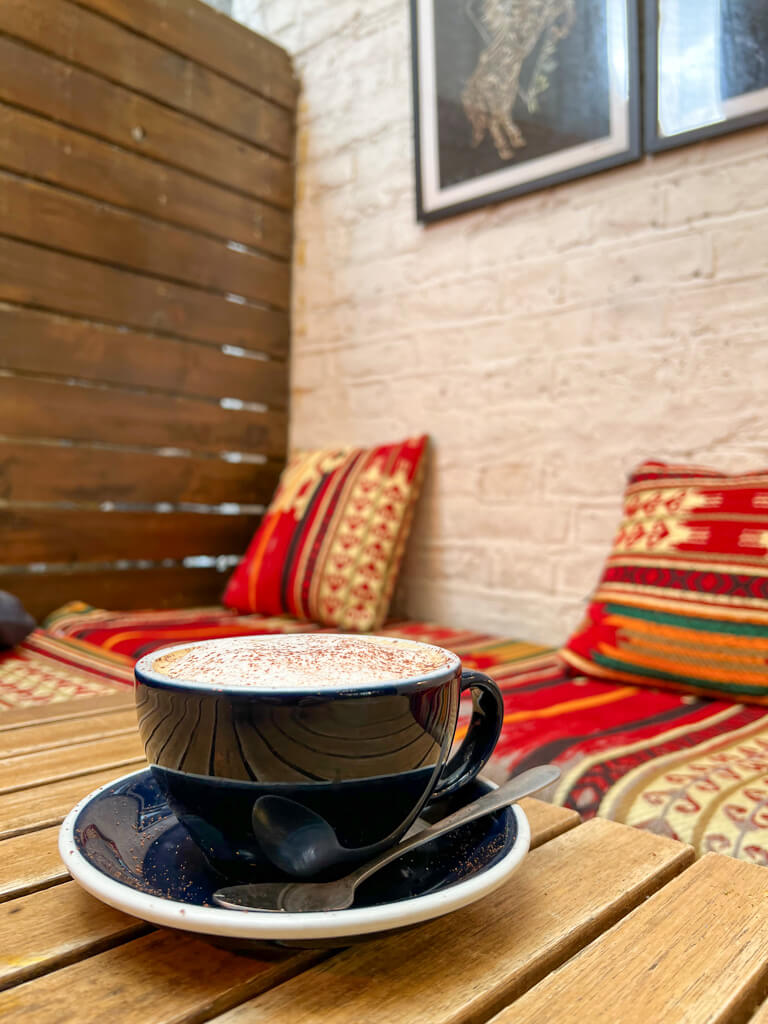 Coffee cup and saucer on a table with colourful cushions in background. Copyright@2024 mapandfamily.com