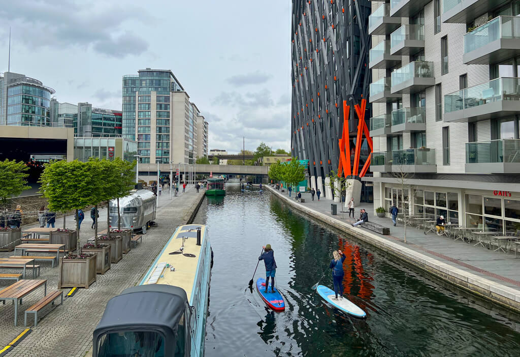Paddleboarders on Grand Union canal with Airstream trailer cafe on left bank and GAIL's bakery to the right. Copyright@2024 mapandfamily.com