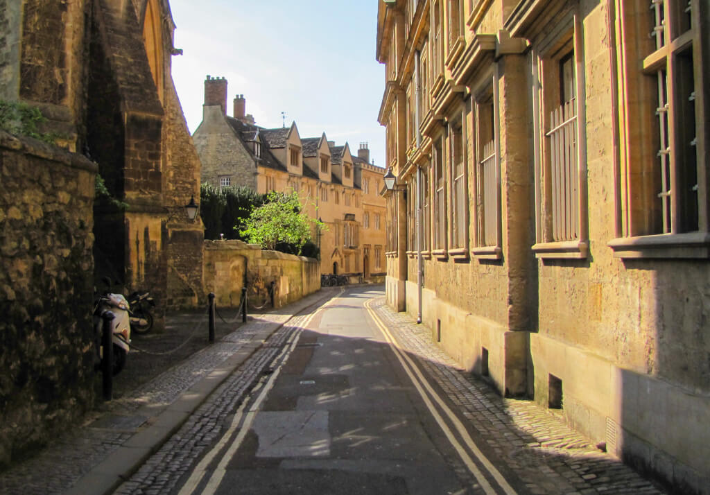 A quiet street in Oxford with historic golden hued buildings on either side.Copyright@2024 mapandfamily.com 