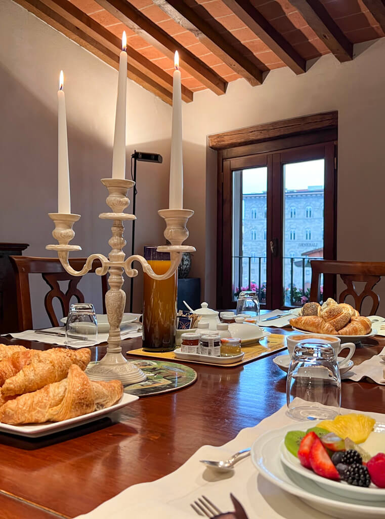 A formal dining table laid for breakfast with pastries, fruit and a silver lighted candelabra. Copyright@2024 mapandfamily.com 