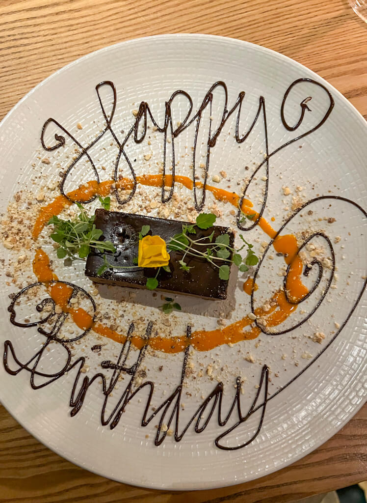 A plate with a chocolate slice and the words Happy Birthday written with a flourish in chocolate sauce. Copyright@2024 Nancy Roberts